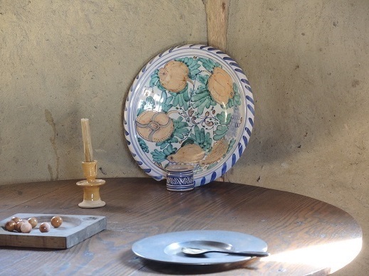 Plate with spoon on it, candle, and painted platter on wooden table top.