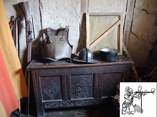 Carved wooden chest with armor on it and matchlock gun leaning against wall beside chest.